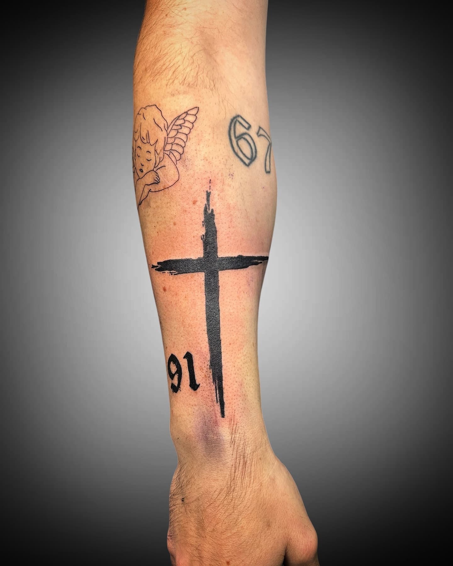 Schwarzes Pinselstrich-Kreuz mit den Zahlen 91 und 67 in Frakturschrift auf dem Unterarm